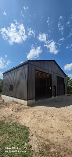Black steel post-frame workshop with timber accents under blue sky
