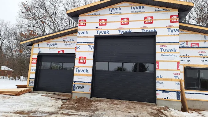 Post-frame building wrapped in Tyvek with black overhead garage doors during construction
